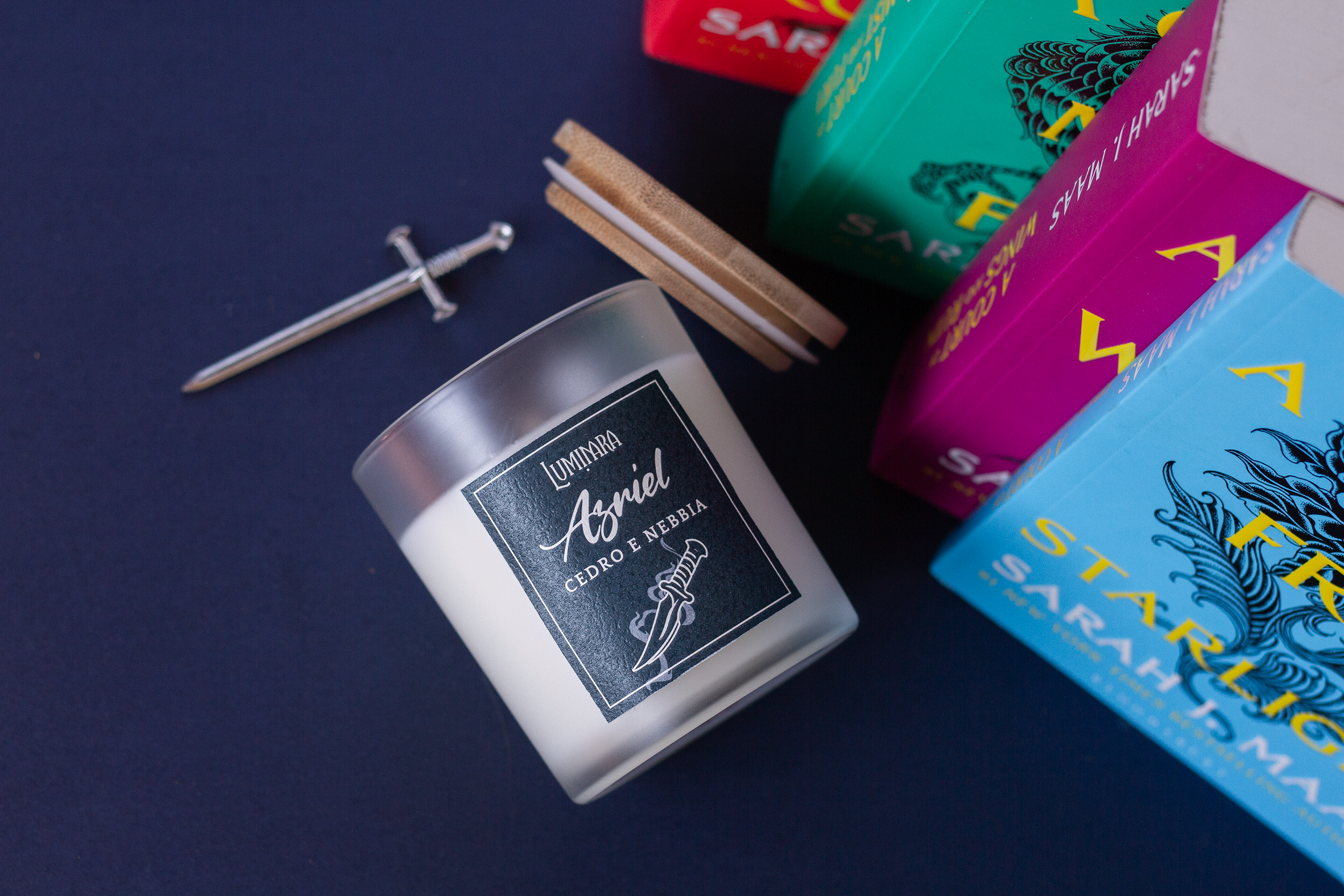 Candela in vetro con coperchio in bamboo, sull'etichetta il nome Azriel e Luminara Portali - Fragranza cedro e nebbia notturna, ispirata allo Spymaster e al Maasverse. sullo sfondo la Serie di libri ACOTAR